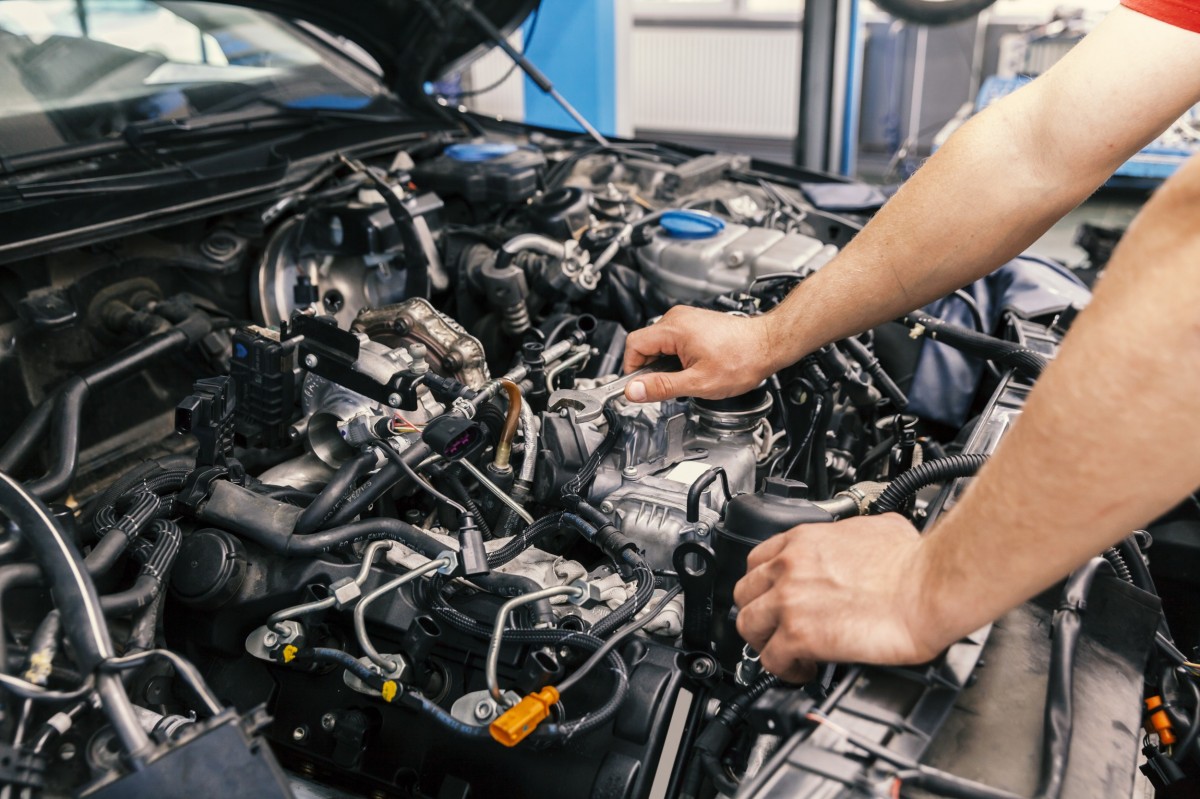 mechanic's hands holding wrench under the hood of a car